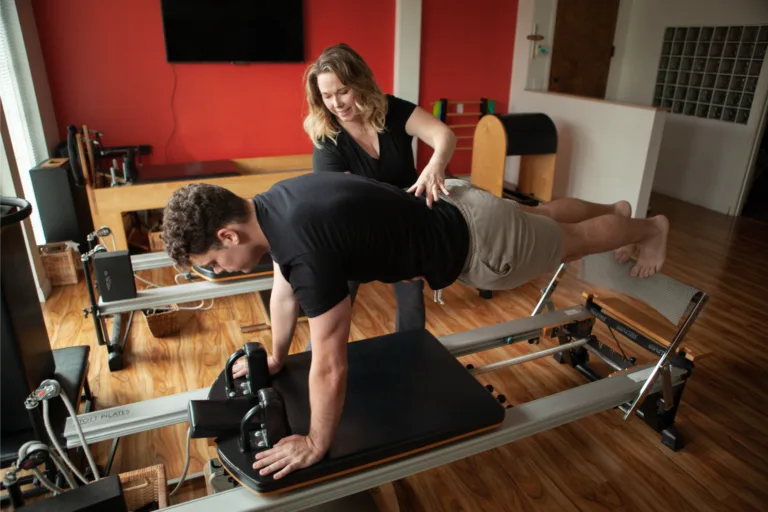 Physical therapist correcting a patient's plank position on a Pilates reformer.