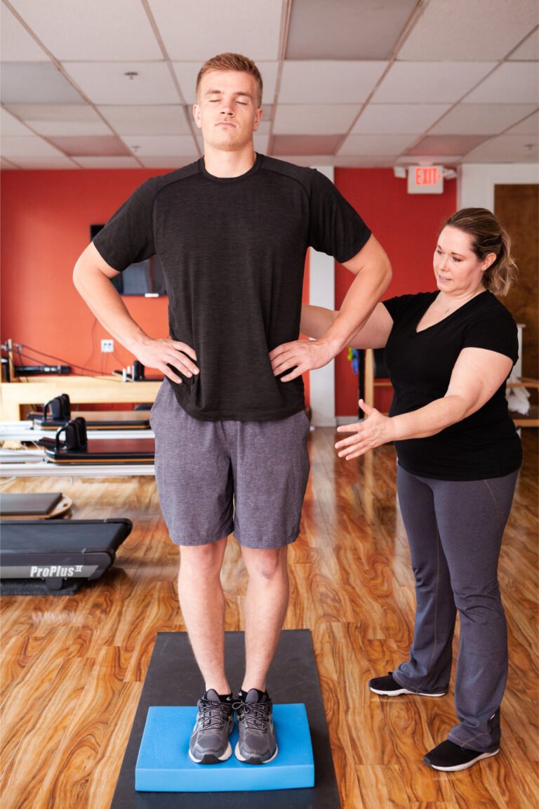 Physical therapist supervising an eyes-closed balance test on a foam pad during a concussion assessment